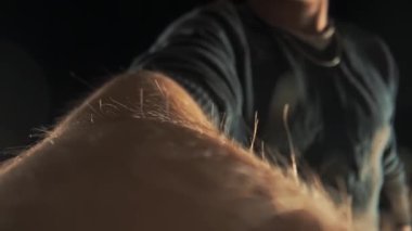 Kamera bir adamın elinin yüzeyinde süzülür. Makro, erkeğin elindeki deri ve saç dokusunu aktarırken çekilmiş. Sinematik ışıklandırmalı koyu arkaplan.