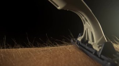 Makro deri ve saç dokusu. Ustura elin üzerinden geçer ve tüyleri traş eder ve arkasında çıplak deri bırakır. Her saç ve deri dokusunu aydınlatan yumuşak ışıkla dolu karanlık bir stüdyo..