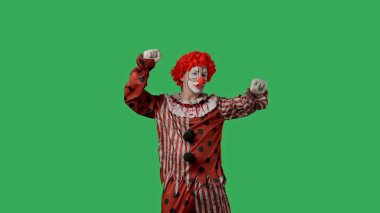 Yeşil ekran krom anahtarlı komik palyaço. Kırmızı peruklu ve takım elbiseli aktör elini sallıyor, sonra hayali bir pikabı açıyor ve mutlu bir şekilde dans etmeye başlıyor. Tatil ve kutlama konsepti.