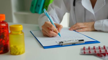 Ofiste çalışan bir tıp uzmanı. Masasında steteskoplu beyaz önlüklü kadın doktor reçete yazıyor, panoya form dolduruyor, yakından bakıyor. Tıbbi tedavi kavramı.