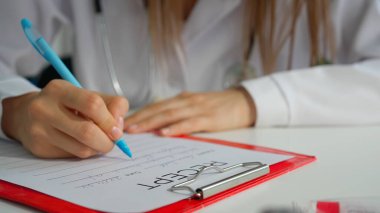 Ofiste çalışan bir tıp uzmanı. Beyaz önlüklü kadın doktor reçeteli reçete yazıyor, panoya tıbbi form dolduruyor, manzarayı kapatıyor. Tıbbi tedavi kavramı.