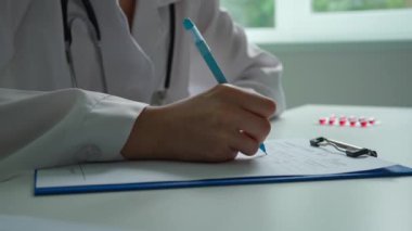 Ofiste çalışan bir tıp uzmanı. Beyaz önlüklü kadın doktor başvuru formu dolduruyor. Hastanın dosyasını dolduruyor. Kapatın. Tıbbi tedavi kavramı.