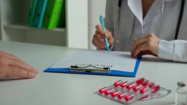 Ofiste çalışan bir tıp uzmanı. Beyaz önlüklü kadın doktor boş reçeteli reçeteyi panoya yazıp hastaya kağıt çarşaf veriyor, yakın çekim yapıyor. Tıbbi tedavi kavramı.