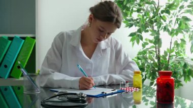Ofiste çalışan bir tıp uzmanı. Beyaz önlüklü kadın doktor başvuru formu dolduruyor, dosyada şarkı söylüyor. Tıbbi tedavi kavramı.
