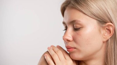 Çekici kadın model güzellik tedavisi yapıyor. Kameraya poz veren genç sarışın kadın, omuzlarına dokunuyor doğal görünüyor, beyaz stüdyo arka planında izole edilmiş yakın plan çekimi. Güzel cilt bakımı konsepti