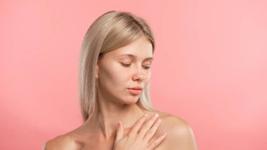 Çekici kadın model güzellik tedavisi yapıyor. Kameraya poz veren genç sarışın kadın, boyuna ve köprücük kemiğine dokunuyor. Pembe stüdyo arka planında izole edilmiş. Güzel cilt bakımı konsepti