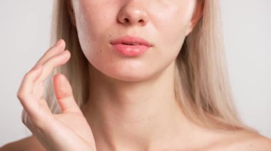 Çekici kadın model güzellik tedavisi yapıyor. Kameraya poz veren genç sarışın kadın, çene yüz hatlarına dokunuyor, beyaz stüdyo arka planında izole edilmiş, yakın çekim. Güzel cilt bakımı konsepti