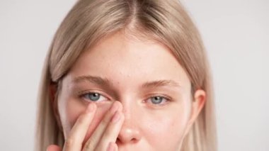 Çekici kadın model güzellik tedavisi yapıyor. Kameraya poz veren genç sarışın kadın, kaşlarına ve gözlerinin altındaki tenine dokunuyor, beyaz stüdyo arka planında izole edilmiş, yakın çekim. Güzel cilt bakımı konsepti