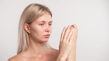 Çekici kadın model güzellik tedavisi yapıyor. Kameraya poz veren genç sarışın kadın, el ve parmaklarına vücut losyonu sürüyor, beyaz stüdyo arka planında izole edilmiş. Güzel cilt bakımı konsepti