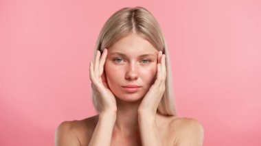 Çekici kadın model güzellik tedavisi yapıyor. Kameraya poz veren genç sarışın kadın, yüz çizgisi ve tapınaklar, pembe stüdyo arka planında soyutlanmış. Güzel cilt bakımı konsepti