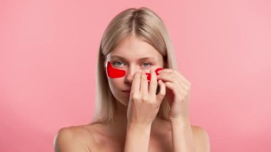 Çekici kadın model güzellik tedavisi yapıyor. Kameraya poz veren genç sarışın kadın, göz bandı takıyor, pembe stüdyo arka planında izole edilmiş. Güzel cilt bakımı konsepti