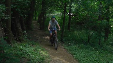Güneşli bir yaz gününde, yeşil bir ormanda bisiklet süren bir adam. Doğada bisikletle seyahat eden bir sporcu. Bisiklet sürmek, sağlıklı yaşam tarzı..