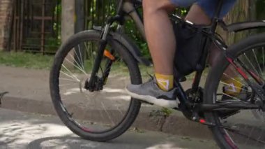 Erkek bir bisikletçi güneşli bir yaz öğleden sonrasında bir parkta bir yolda bisikletine biner. Erkek bacakları pedal çeviriyor ve tekerlekleri çeviriyor. Sağlıklı yaşam tarzı.