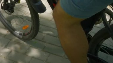 Erkek bir bisikletçi güneşli bir yaz öğleden sonrasında bir parkta bir yolda bisikletine biner. Erkek bacakları pedal çeviriyor ve tekerlekleri çeviriyor. Sağlıklı yaşam tarzı.