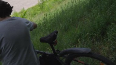 Parkta elinde bisikletle yürüyen bir adam. Güneşli bir yaz gününde yeşil bir parkta yürüyen bir bisikletçi. Sağlıklı yaşam tarzı