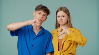 Stüdyoda poz veren genç adam ve kadın. Yeşil arka planda izole edilmiş sarı mavi elbiseli iki genç erkek arkadaş ve kız arkadaş, kameraya üzgün yüzler gösteriyorlar..