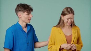 Stüdyoda poz veren genç adam ve kadın. Yeşil arka planda izole edilmiş sarı mavi elbiseli iki genç sevgili, ağlayan adam onu rahatlatıyor ve sarılıyor..