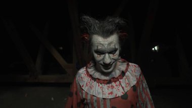 Karanlıkta çatıda korkunç deli bir palyaço. Mahvolmuş evde makyajlı palyaço kılığındaki manyak katil kameraya bakıyor, konuşuyor, gülümsüyor ve çıldırıyor. Cadılar Bayramı gerilim konsepti.