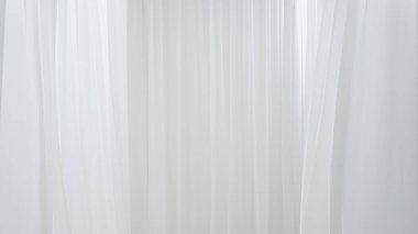 Beyaz ipek kumaşlar, video stüdyosundaki hava vantilatörünün rüzgarı tarafından yavaş yavaş uçuyor ve hareket ediyor. Nesne yerleştirmek için boş bir alan. Soyut beyaz kumaş arka planı. Güzellik konsepti.