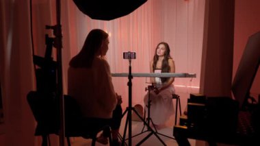 Stüdyoda film çeken bir kadın. Sahne arkasında oturan ve konuşan kadın modeller stüdyoda pembe kumaş arka planlı akıllı telefondan podcast yapan kadın asistanlar. Güzellik blogcusu kavramı.