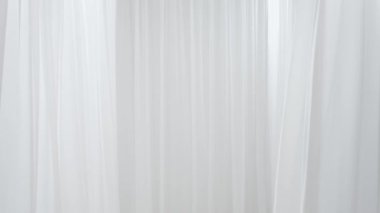 Beyaz ipek kumaşlar, video stüdyosundaki hava vantilatörünün rüzgarı tarafından yavaş yavaş uçuyor ve hareket ediyor. Nesne yerleştirmek için boş bir alan. Soyut beyaz kumaş arka planı. Güzellik konsepti.