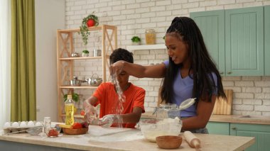 Afro-Amerikalı mutlu aile mutfakta yemek hazırlıyor. Anne ve oğlu pizza hamuru yoğurmak için masaya un serperler. Birlikte vakit geçirip, sağlıklı bir hayat sürüyoruz..