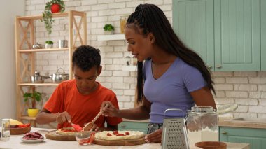 Afro-Amerikalı mutlu aile mutfakta yemek hazırlıyor. Anne ve oğul bitmemiş pizzalarının dibine sosis dilimleri koyuyorlar. Birlikte vakit geçirip, sağlıklı bir hayat sürüyoruz..