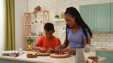 Afro-Amerikalı mutlu aile mutfakta yemek hazırlıyor. Anne ve oğul bitmemiş pizzalarının dibine sosis dilimleri koyuyorlar. Birlikte vakit geçirip, sağlıklı bir hayat sürüyoruz..