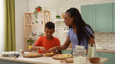 Afro-Amerikalı mutlu aile mutfakta yemek hazırlıyor. Anne ve oğlu pizzaya peynir serpiyor. Sevinçle beşlik çakın. Birlikte vakit geçirip, sağlıklı bir hayat sürüyoruz..