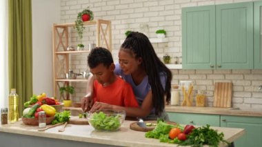 Afro-Amerikalı mutlu aile mutfakta yemek hazırlıyor. Annem salata için salatalık doğramaya yardım ediyor. Birlikte zaman geçirmek, sağlıklı bir yaşam tarzı..