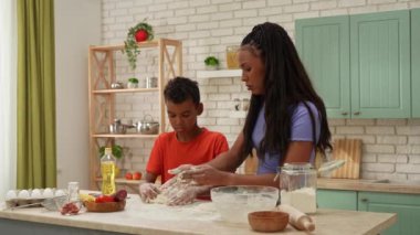 Afro-Amerikalı mutlu aile mutfakta yemek hazırlıyor. Anne, oğlunun pizza için mutfak masasında hamur yoğurmasına yardım ediyor. Birlikte vakit geçirip, sağlıklı bir hayat sürüyoruz..