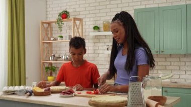 Afro-Amerikalı mutlu aile mutfakta yemek hazırlıyor. Oğlum, annenin pizza için domates dilimleyişini izliyor. Birlikte vakit geçirip, sağlıklı bir hayat sürüyoruz..