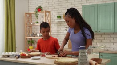 Afro-Amerikalı mutlu aile mutfakta yemek hazırlıyor. Oğlum, annenin pizza için sosis dilimleyişini izliyor. Birlikte vakit geçirip, sağlıklı bir hayat sürüyoruz..