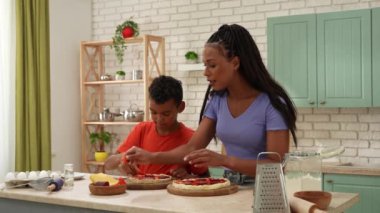Afro-Amerikalı mutlu aile mutfakta yemek hazırlıyor. Anne ve oğul bitmemiş pizzalarının dibine domates dilimleri koyuyorlar. Birlikte vakit geçirip, sağlıklı bir hayat sürüyoruz..