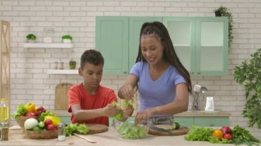 Afro-Amerikalı mutlu aile mutfakta yemek hazırlıyor. Anne ve oğlu salata hazırlıyor ve yeşil salata yapraklarını parçalıyor. Birlikte zaman geçirmek, sağlıklı bir yaşam tarzı..