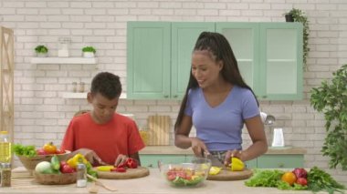 Afro-Amerikalı mutlu aile mutfakta yemek hazırlıyor. Annem salata için kırmızı biber doğramaya yardım ederken, o da sarı biber dilimliyor. Birlikte zaman geçirmek, sağlıklı bir yaşam tarzı..