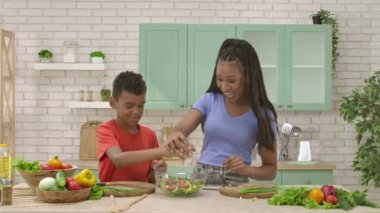 Afro-Amerikalı mutlu aile mutfakta yemek hazırlıyor. Anne ve oğul salataya tuz ve yağ ekliyor, sonra çak bir beşlik. Birlikte zaman geçirmek, sağlıklı bir yaşam tarzı..
