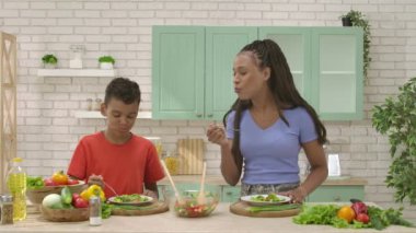 Afro-Amerikalı mutlu aile mutfakta yemek hazırlıyor. Anne oğul salata tadıyor, çak bir beşlik. Birlikte zaman geçirmek, sağlıklı bir yaşam tarzı..