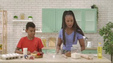 Afro-Amerikalı mutlu aile mutfakta yemek hazırlıyor. Anne oğluna pizza yapmak için ihtiyacı olan malzemeleri ve çatal bıçakları gösteriyor. Birlikte vakit geçirip, sağlıklı bir hayat sürüyoruz..