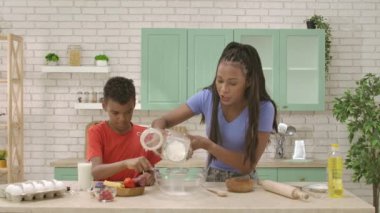 Afro-Amerikalı mutlu aile mutfakta yemek hazırlıyor. Annem klozete un ekliyor ve oğluna un elemeyi öğretiyor. Birlikte vakit geçirip, sağlıklı bir hayat sürüyoruz..