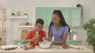 Afro-Amerikalı mutlu aile mutfakta yemek hazırlıyor. Anne ve oğlu hamur karışımına yağ döküp karıştırmaya başladılar. Birlikte vakit geçirip, sağlıklı bir hayat sürüyoruz..