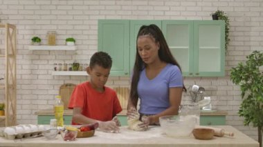 Afro-Amerikalı mutlu aile mutfakta yemek hazırlıyor. Anne, oğlunun pizza için mutfak masasında hamur yoğurmasına yardım ediyor. Birlikte vakit geçirip, sağlıklı bir hayat sürüyoruz..