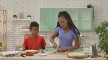 Afro-Amerikalı mutlu aile mutfakta yemek hazırlıyor. Oğlum, annenin pizza için sosis dilimleyişini izliyor. Birlikte vakit geçirip, sağlıklı bir hayat sürüyoruz..