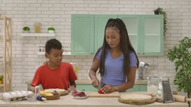 Afro-Amerikalı mutlu aile mutfakta yemek hazırlıyor. Oğlum, annenin pizza için domates dilimleyişini izliyor. Birlikte vakit geçirip, sağlıklı bir hayat sürüyoruz..