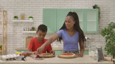 Afro-Amerikalı mutlu aile mutfakta yemek hazırlıyor. Anne ve oğul bitmemiş pizzalarının dibine sosis dilimleri koyuyorlar. Birlikte vakit geçirip, sağlıklı bir hayat sürüyoruz..
