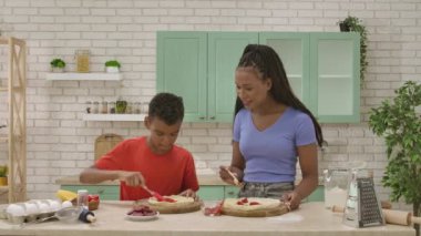Afro-Amerikalı mutlu aile mutfakta yemek hazırlıyor. Anne ve oğul bitmemiş pizzalarının dibine sosis dilimleri koyuyorlar. Birlikte vakit geçirip, sağlıklı bir hayat sürüyoruz..