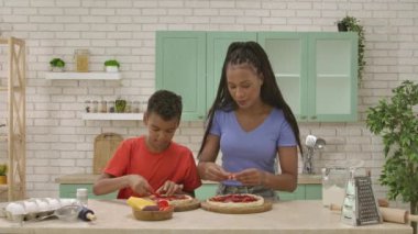 Afro-Amerikalı mutlu aile mutfakta yemek hazırlıyor. Anne ve oğul bitmemiş pizzalarının dibine domates dilimleri koyuyorlar. Birlikte vakit geçirip, sağlıklı bir hayat sürüyoruz..