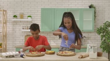 Afro-Amerikalı mutlu aile mutfakta yemek hazırlıyor. Anne ve oğlu pizzaya peynir serpiyor. Sevinçle beşlik çakın. Birlikte vakit geçirip, sağlıklı bir hayat sürüyoruz..