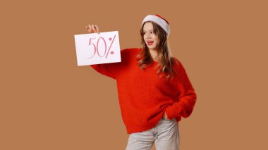Kırmızı kazaklı Kar Kızı ve bej arka planda bir stüdyoda poz veren yeni yıl şapkası. Genç kızda% 50 indirim var. Yeni yıl ve Noel tatili kavramı.