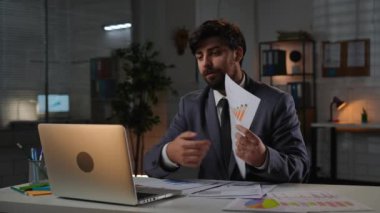 Odaklanmış profesyonel erkek, geç saatlere kadar çalışıyor. Yetişkin iş adamı yöneticisi masa başında oturuyor ofiste fazla mesai yapıyor, video görüşmeleri ile konuşuyor, kızgın ifadeler, bilgi içeren kağıtları yırtıyor..